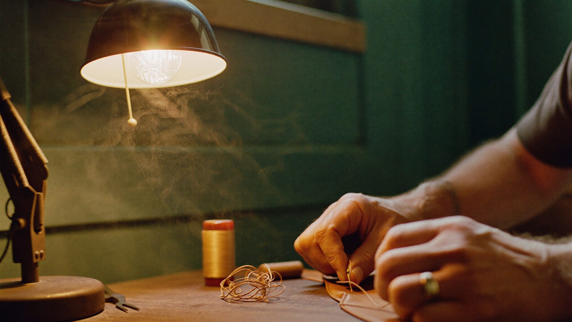 Craftsman's hands stitching leather at a workbench